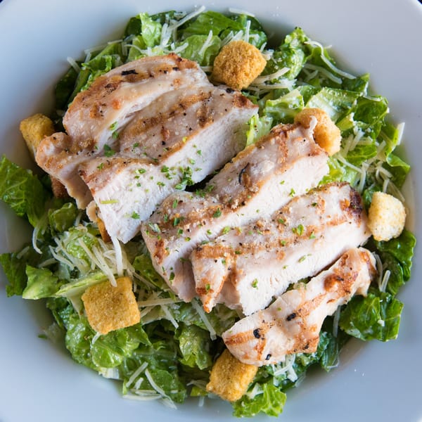 Grilled chicken Caesar salad with croutons and parmesan cheese in a white bowl.