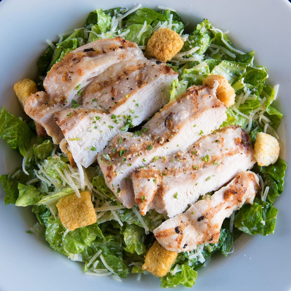 Grilled chicken Caesar salad with croutons and parmesan cheese in a white bowl.