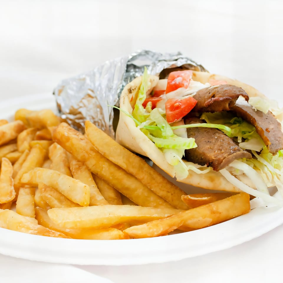 A gyro wrapped in foil with fries on a white plate from AJ's Pizza, Subs, and Wings.